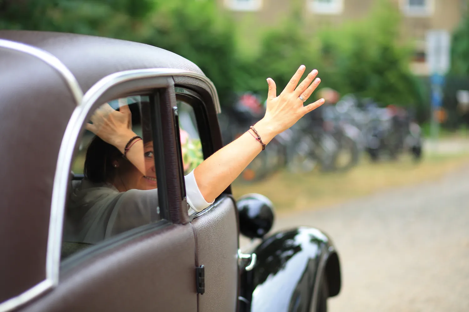 Brautpaar winkt zum Abschied aus dem Auto